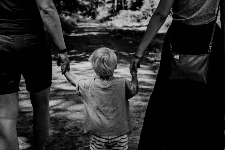 Ein kleiner Junge hält beide seiner Eltern an den Händen, Blick von hinten.